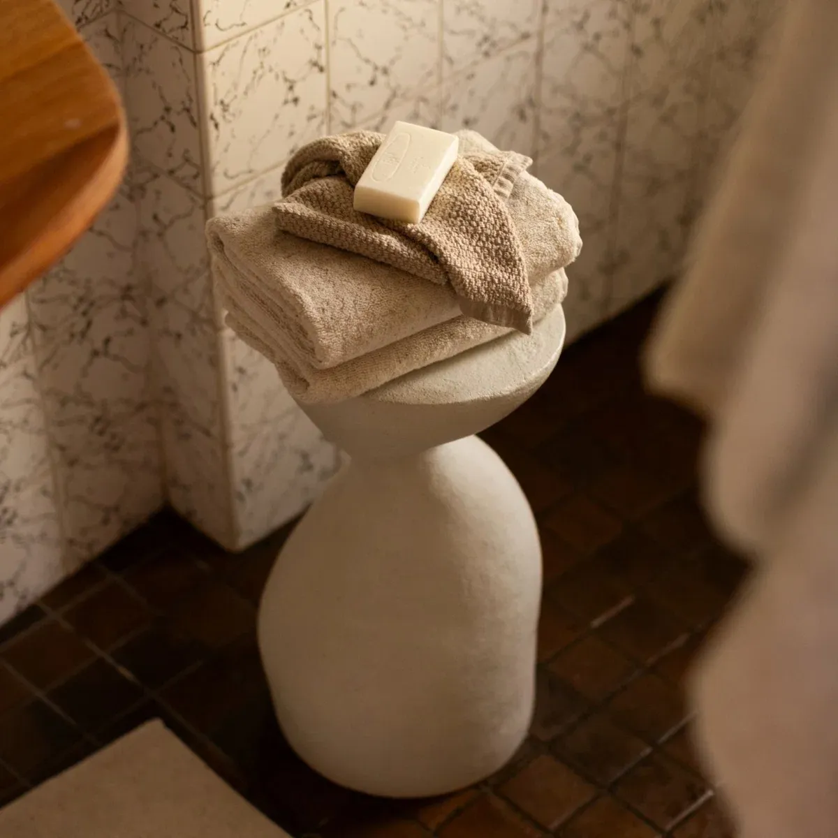 Folded beige towels and a bar of soap on a sculptural bathroom pedestal